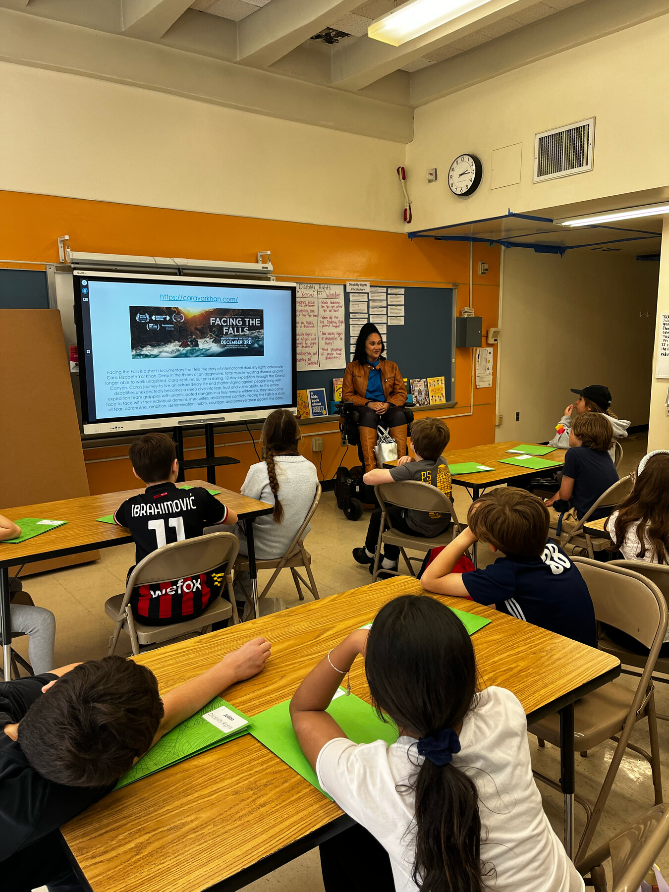 Cara Yar Khan speaking with Grade 5 students seated around classroom tables at PS 234.
